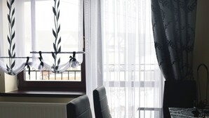Un coin repas avec une table et des chaises, une fenêtre ornée de rideaux légers et une vue sur l’extérieur.