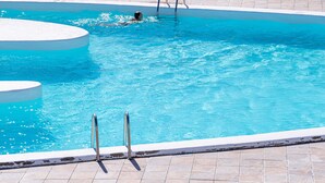 Ein Schwimmbecken mit gefliestem Sonnendeck und Metallleitern.