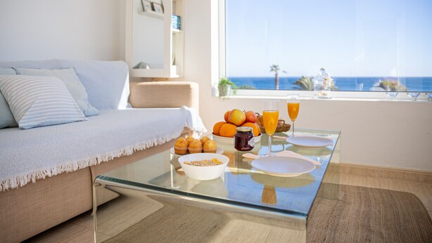 Ein modernes Wohnzimmer mit einem Glastisch, einer Couch und Blick aufs Meer.
