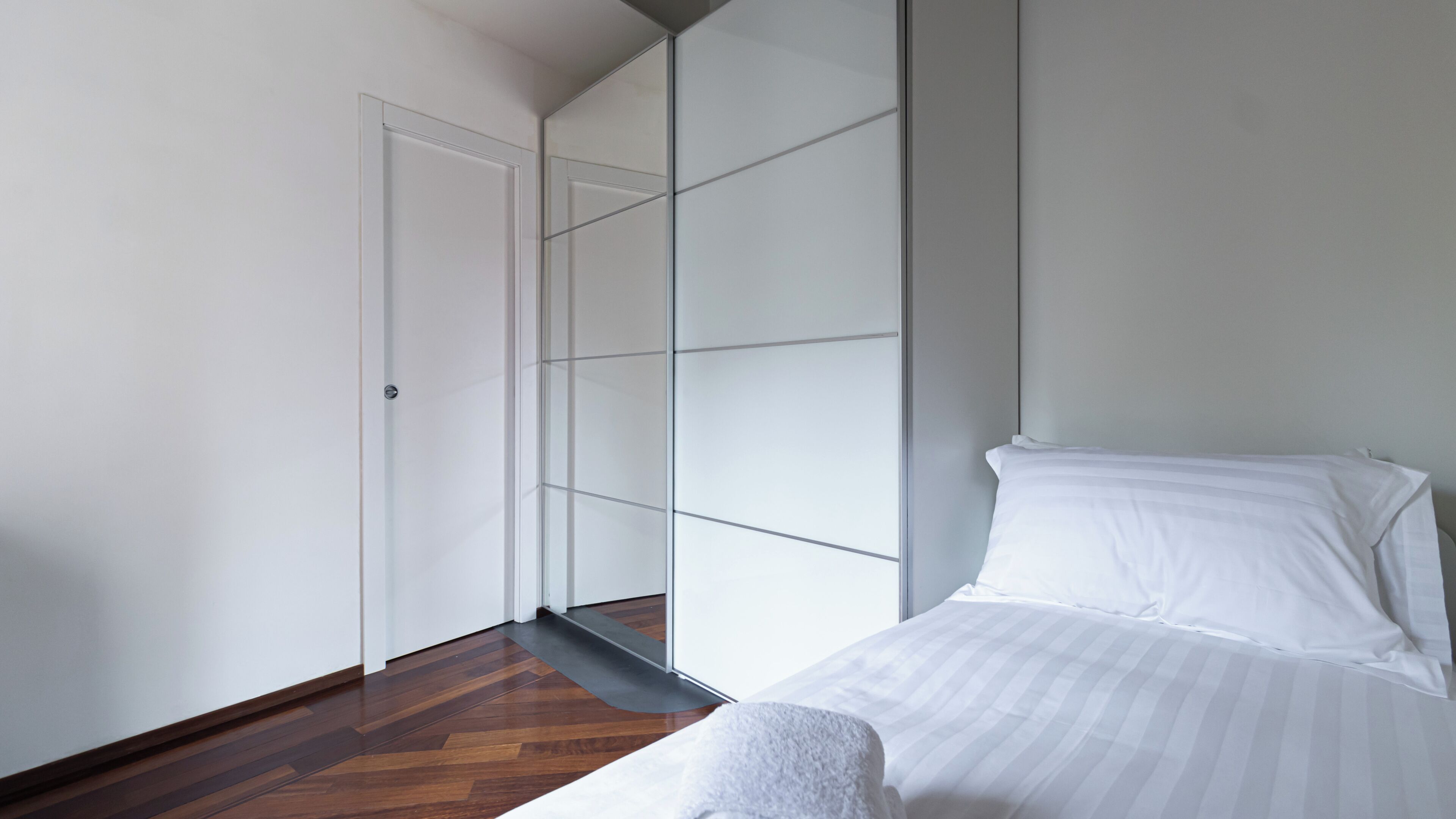 A bedroom with a bed, a wooden floor, a white door, and a glass partition wall.