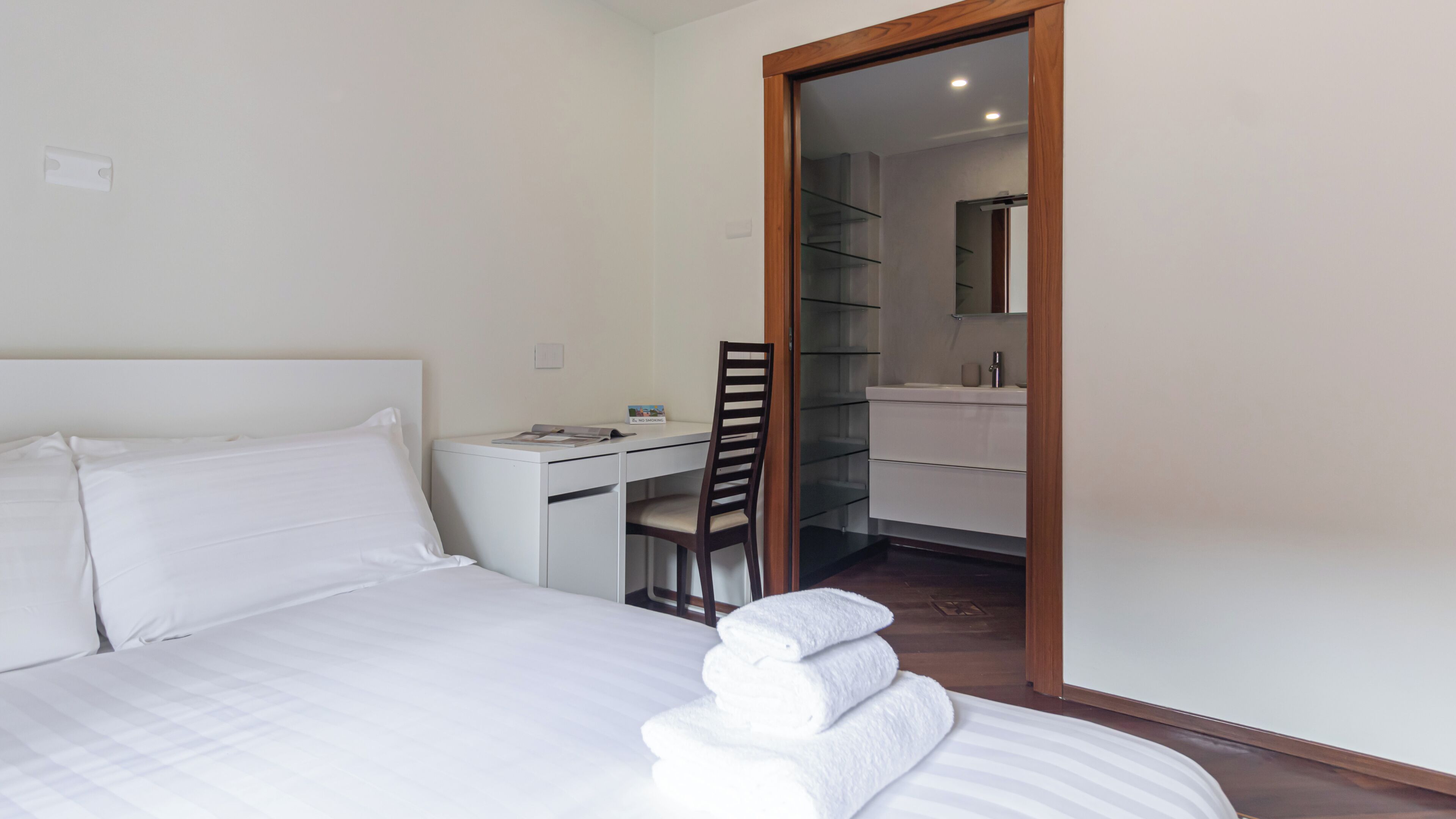Een hotelkamer met een bed, een bureau, een stoel en een badkamer zichtbaar door een geopende deur.