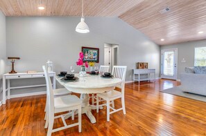 A dining area with a round table, white chairs, and a white pendant light. There is a painting on the wall and a door leading to another room. - Came & Stayed, Community Pool, Tranquility, Beach Gear Credit Included! (St George Island)