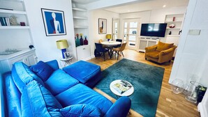 Una sala de estar moderna con un sofá azul, un comedor con mesa y sillas, un televisor y una zona de cocina con armarios y un microondas.