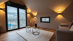 A modern living room with a large window, two geometric tables, a white rug, and a grey sofa.