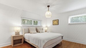 Un dormitorio con cama, mesitas de noche, lámpara colgante y ventanas con persianas.