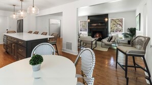 Una cocina moderna con una isla central, comedor con mesas redondas y sala de estar con chimenea.