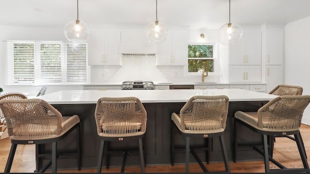 Una cocina moderna con una isla central, cuatro sillas de mimbre e iluminación colgante.