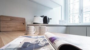 Una cucina con un piano di lavoro in legno, due tazze bianche con marchio Italianway, un bollitore bianco e una finestra vista balcone.