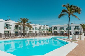 Une piscine entourée de bâtiments blancs dotés de balcons, de palmiers et de chaises longues.