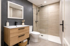 A modern bathroom with a white vanity, a toilet, and a glass-enclosed shower.