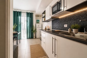 A modern kitchen with white cabinets, a black countertop, a built-in microwave, and a stone backsplash.