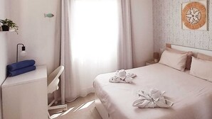 Een slaapkamer met een bed, een bureau, een stoel, een raam met gordijnen en een wanddecoratie.