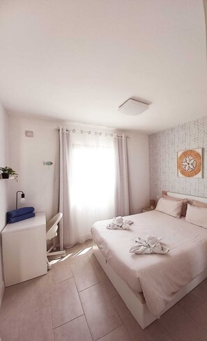 Une chambre Ă coucher comprenant un lit, un bureau, une chaise, une fenĂȘtre avec des rideaux et une Ćuvre dâart accrochĂ©e au mur.