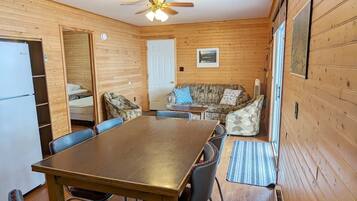 A cozy cabin with a wooden interior, a dining table with chairs, a sofa, and a ceiling fan.