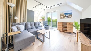 A modern living room with a grey sectional sofa, a wooden coffee table, and a TV stand. - Apartamenty Sun & Snow Na Różanej (Ustronie Morskie)