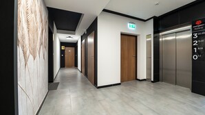 A modern hallway with a wooden door marked with the number 26, an emergency exit sign, and an elevator with a digital display showing floor numbers. - Apartamenty Sun & Snow Na Różanej (Ustronie Morskie)