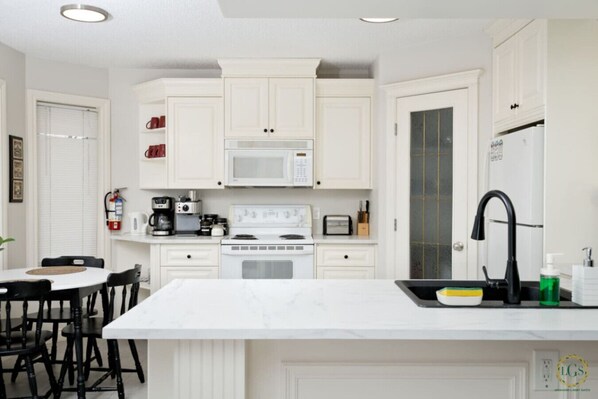 Una cocina moderna con armarios blancos, una isla central, microondas, estufa y un lavamanos con grifo negro.