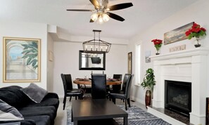 A living room with a fireplace, a dining table, and a ceiling fan.