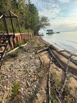 Une plage avec une structure en bois, un rivage rocheux et un bâtiment situé au loin, près de l’eau.