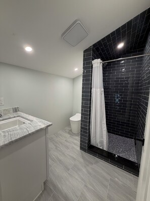 Un baño moderno con lavamanos de mármol, inodoro y zona de ducha con azulejos negros.