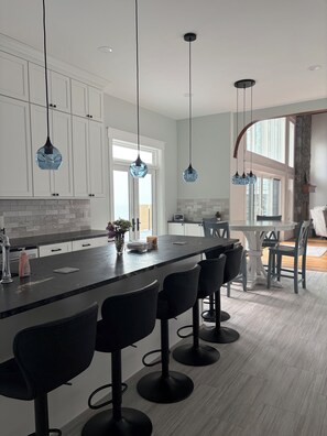 A modern kitchen with a central island, bar stools, pendant lighting, and a view to the dining area.