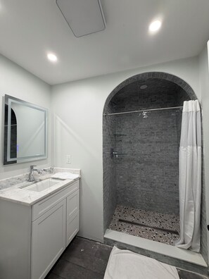 Une salle de bain avec un meuble-lavabo en marbre, une douche avec un mur en briques et un rideau de douche blanc.