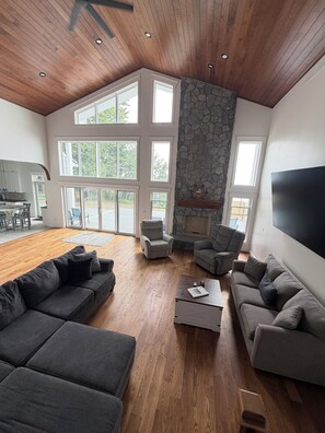 Un salón amplio con chimenea de piedra, ventanas grandes y un televisor de pantalla plana.