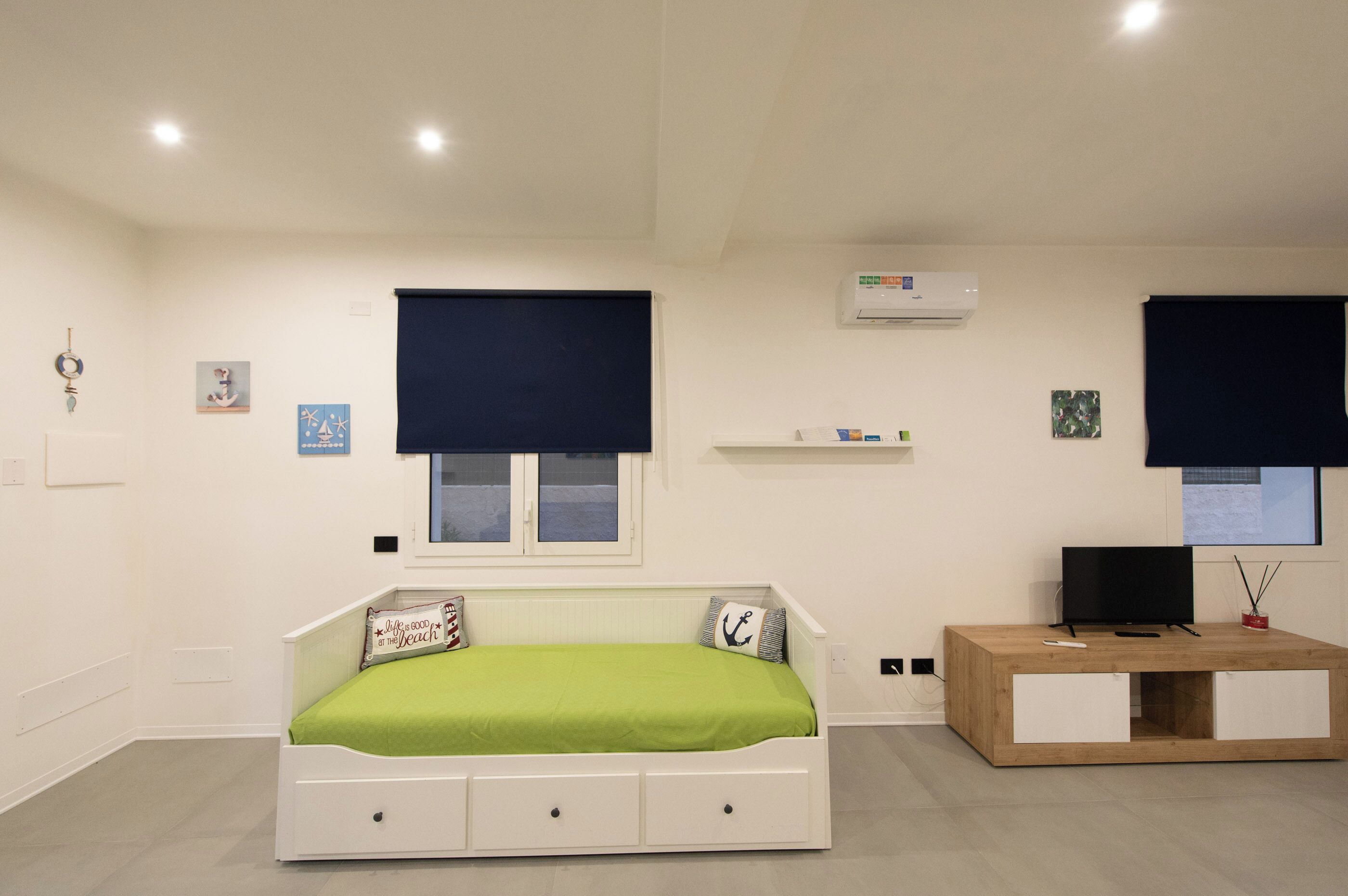 A bedroom with a bed, a TV, a small wooden cabinet, and a window with a blind.