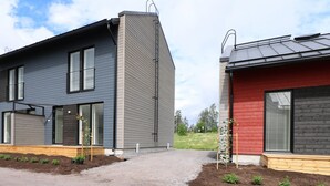 A modern two-story house with a grey exterior, a red section on the right, and a wooden deck with small plants. - Forenom Serviced Apts Espoo Perusmäki 2 (Espoo)