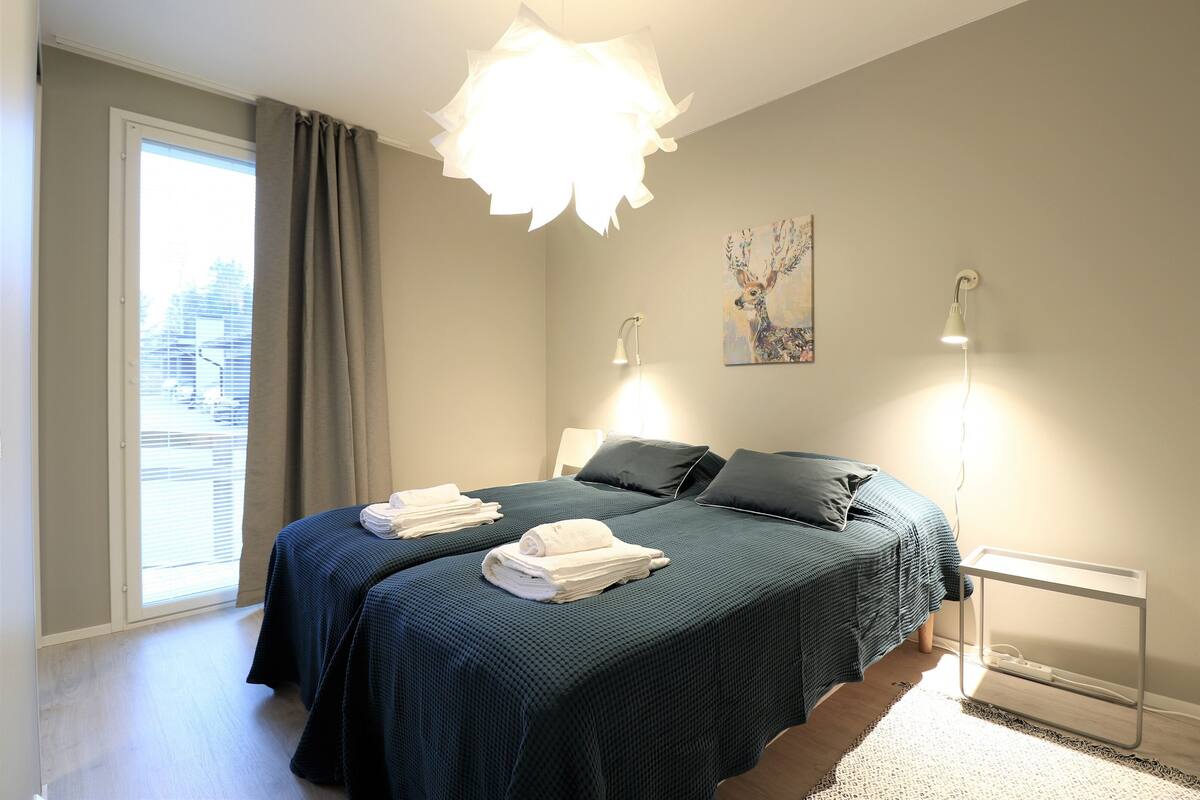Un dormitorio con dos camas, un ventanal con cortinas, una lámpara de pared y un cuadro.