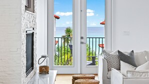 Un salon moderne avec une cheminée blanche, un canapé blanc et un balcon offrant une vue sur la mer.