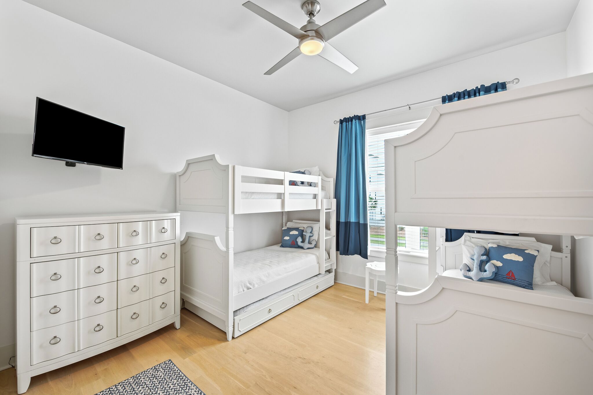 Une chambre avec un lit superposé, une commode, un téléviseur et un ventilateur de plafond.