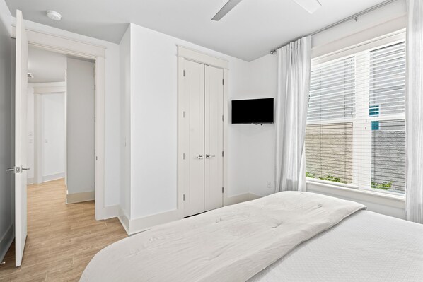 A bedroom with a bed, a TV mounted on the wall, and a window with blinds.