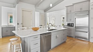 Une cuisine moderne avec des meubles gris, des appareils en acier inoxydable et un îlot central doté de tabourets.