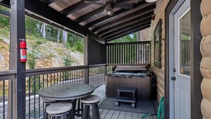A covered outdoor area with a hot tub, a table with stools, and a fire extinguisher.