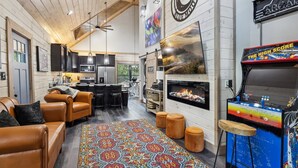 A cozy living room with leather sofas, a colorful rug, a fireplace, and a retro arcade machine.
