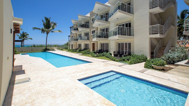 A modern hotel with a pool area, multiple balconies, and a view of the ocean. - 0048 Affordable Condo in the Beach (Cabarete)