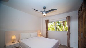 A bedroom with a bed, nightstands, a ceiling fan, a window with curtains, and a wardrobe. - 0048 Affordable Condo in the Beach (Cabarete)