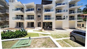 A modern multi-story building with balconies, a central courtyard, and a car parked nearby. - 0048 Affordable Condo in the Beach (Cabarete)