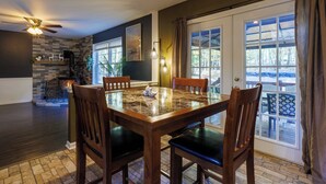 Un comedor con una mesa y sillas de madera, una chimenea y vistas al exterior a través de amplios ventanales.