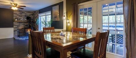 A dining area with a wooden table and chairs, a fireplace, and a view of the outdoors through large windows.