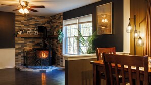 Un comedor con chimenea de ladrillo, ventilador de techo y ventana con persianas.