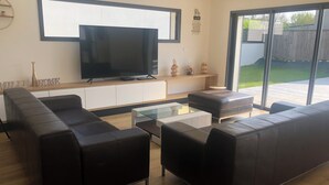 A modern living room with a large flat-screen TV, leather sofas, a glass coffee table, and a sliding glass door leading to a patio. - Seaside villa PMR standard Portsall (Ploudalmézeau)