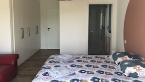 A bedroom with a bed, a red chair, a wardrobe, and a shower area. - Seaside villa PMR standard Portsall (Ploudalmézeau)