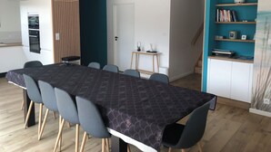 A modern dining area with a long table, chairs, a pendant light, a small side table, and a bookshelf. - Seaside villa PMR standard Portsall (Ploudalmézeau)