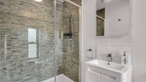 Un bagno moderno con doccia vetro, lavandino bianco e specchio sopra il lavandino.