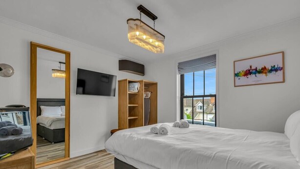 Una camera d'albergo moderna con un ampio letto, una televisione, un armadio in legno e un dipinto con una veduta urbana.