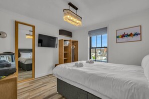 A modern hotel room with a large bed, a television, a wooden wardrobe, and a cityscape painting. - Church View a Tranquil Space for Two - Pass the Keys (Chartham)