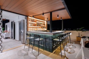 A modern outdoor bar area with a tiled backsplash, bar stools, and a view of the city at night.
