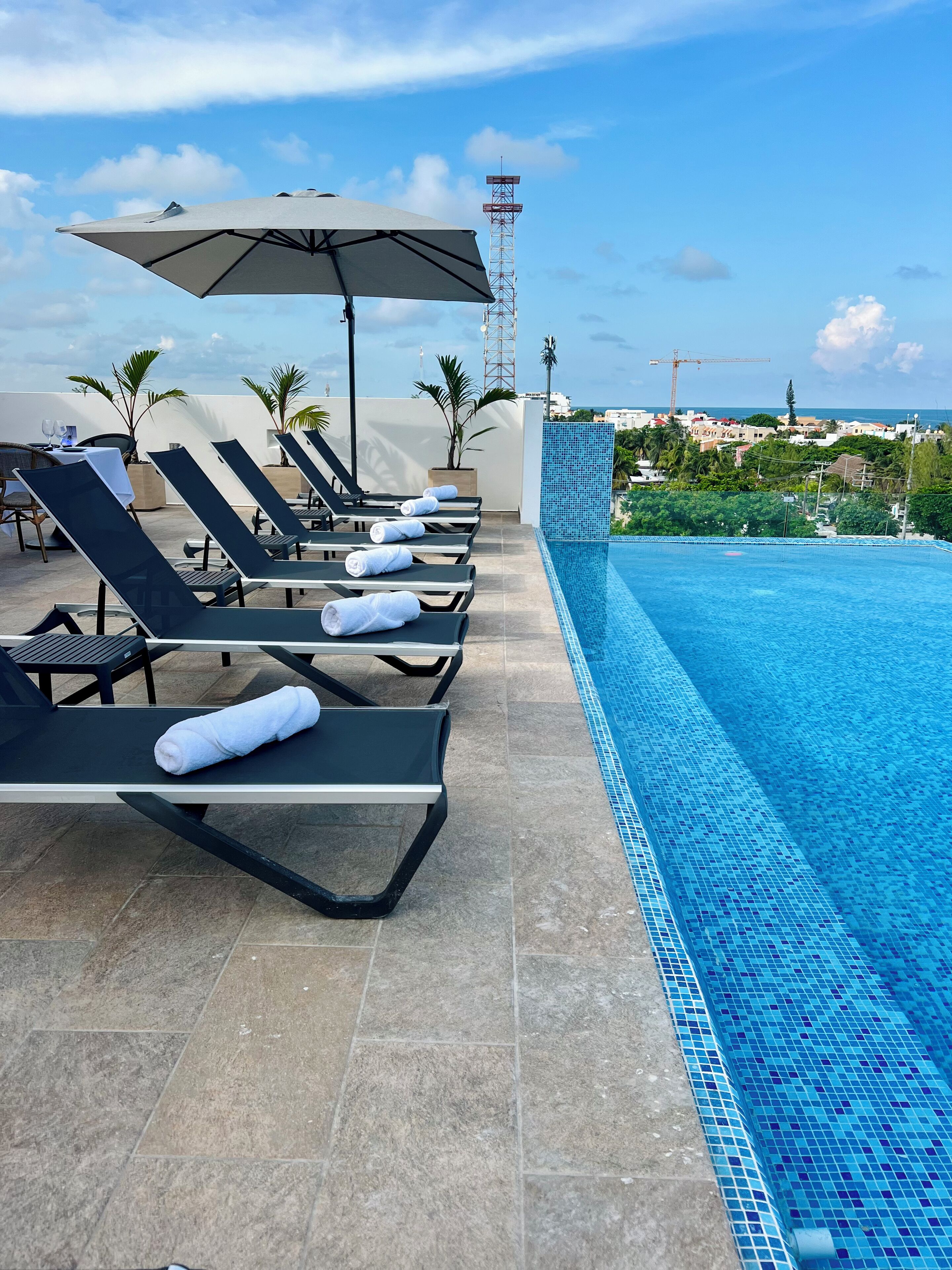 Zona junto a la piscina con tumbonas, piscina con baldosas y vistas al paisaje urbano.